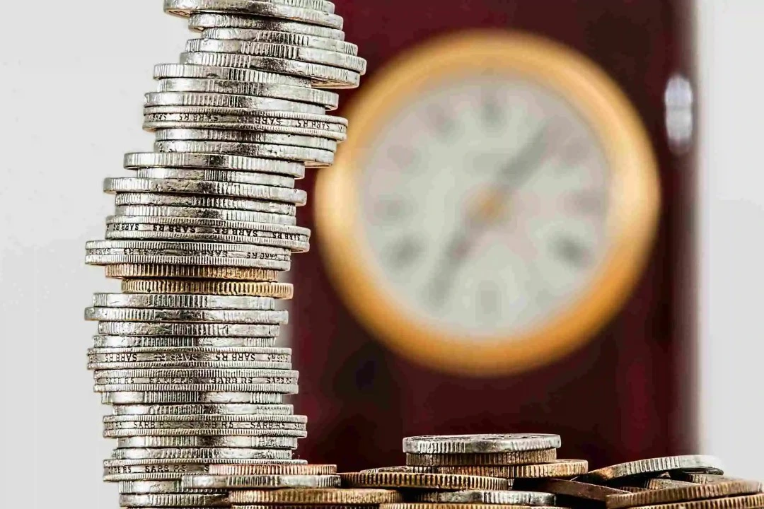 Stack of Coins with a Clock in the background