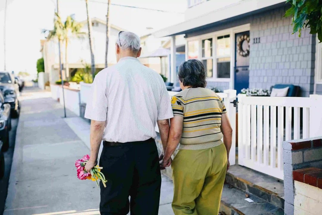 elderly couple walking on a sidewalk with a house and palm trees background 