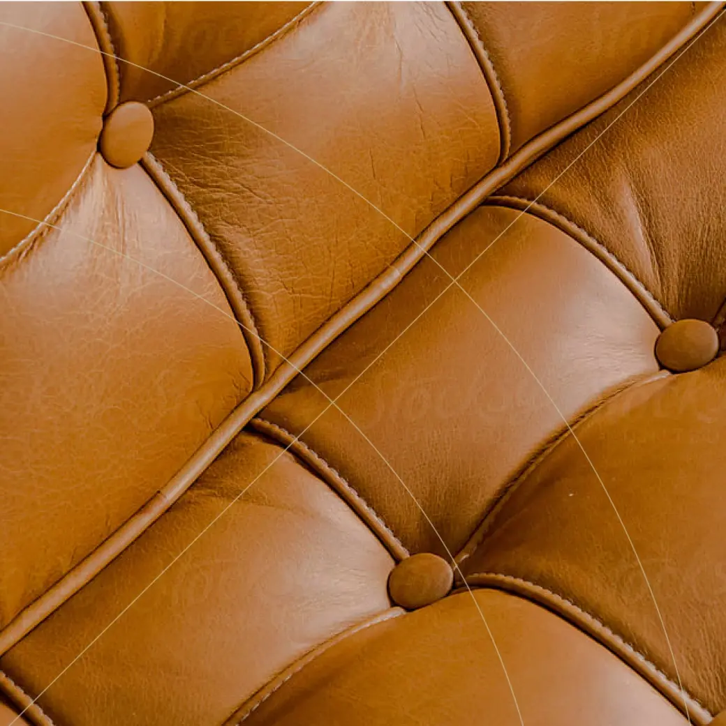Close-up of brown leather upholstery with button-tufted stitching, showing texture, seams, and natural creases in the material.