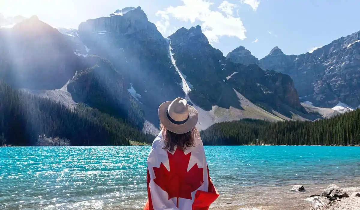 Girl wearing a hat with a Canada flag on her back facing lake and hills