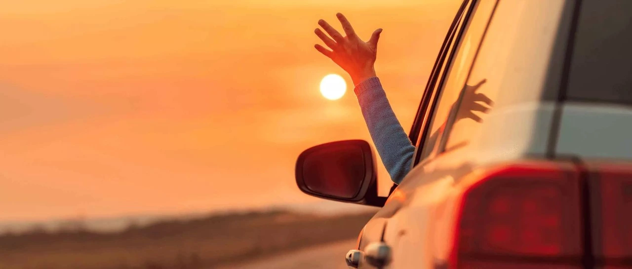 person driving with his hand out the window with a beach background 